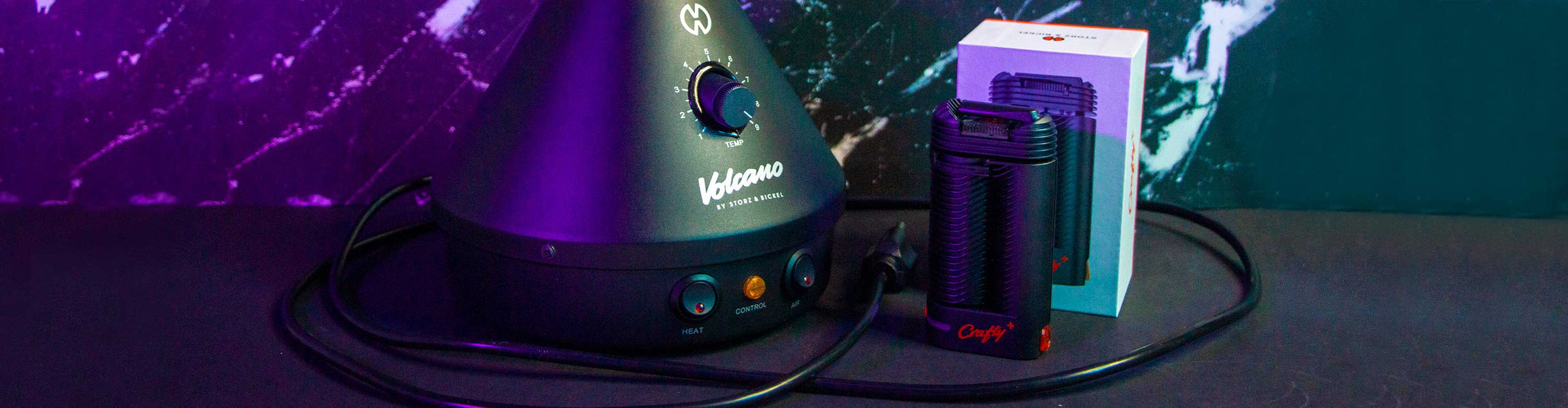Wholesale Storz & Bickel vaporizers Crafty Plus and Volcano resting on a dark table with a lightning background in purple and teal lighting.